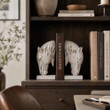 Load image into Gallery viewer, Set of two rustic white horse head bookends holding books on a dark wood shelf.
