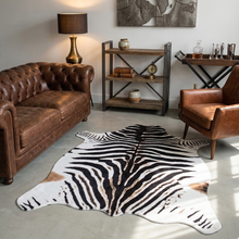 Load image into Gallery viewer, Faux zebra print rug in modern living room with brown leather furniture and rustic decor
